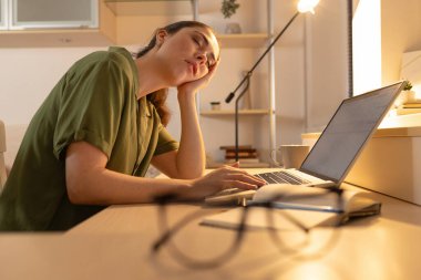 Yorgun genç bir kadın elinde bir dizüstü bilgisayarla masasında oturuyor ve uykuya dalıyor. Çok çalışmaktan dolayı yorgunluk. Öğrenci bilgisayarın yanında uyuyakalıyor. Önplanda bulanık gözlük.