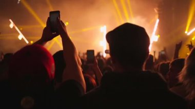 Müzikal rock konserindeki insanlar müzikle el sallıyor. Kulüp atmosferi, turuncu-beyaz ışık ışınları. Dikiz aynası. Eğlence konsepti.