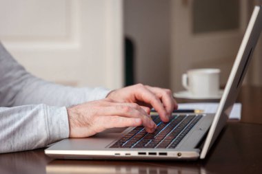 Erkek ellerinin kağıda kalemle yazıp dizüstü bilgisayar kullanışının yan görüntüsü. Modern uzaktan kumanda ve iş. Klavyede parmak yazılıyor.