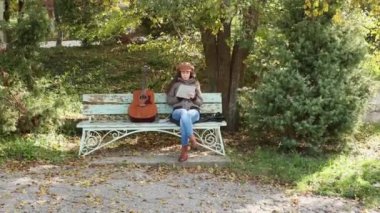 Kafkasyalı güzel bir kadın elinde gitarla bankta oturuyor ve not defterinde notlar üzerinde çalışıyor. Müzik aletleri çalmayı öğrenmek.