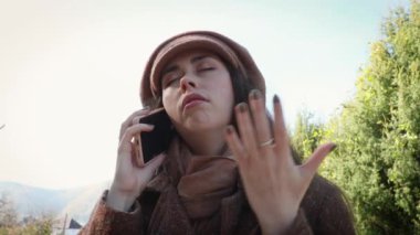 Şapkalı ve paltolu genç bir beyaz kadının portresi telefonda öfkeyle konuşuyor. Öfke, kızgınlık ve dargınlık duyguları. Alt manzara. Psikoloji kavramı