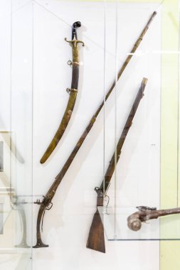 Karmaşık ahşap desenli dekore edilmiş antika bir silah. Vitrinde antika tabancalar ve kılıçlar var. Müzede sergileniyor. Dikey yönelim.