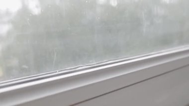 Pencere pervazı olan beyaz bir pencere çerçevesi, su birikintisi yayıyor. Çift camlı pencerede bir boşluk var, pencere çerçevesi sızdırıyor. Jib çekimi