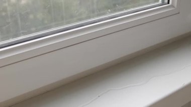 Pencere pervazı olan beyaz bir pencere çerçevesine yakın plan, su birikintisi yayıyor. Çift camlı pencerede bir boşluk var, pencere çerçevesi sızdırıyor..