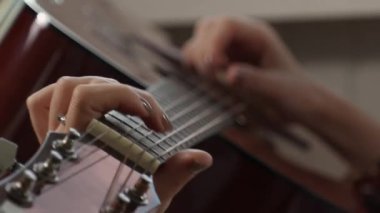 Dişi eller gitar çalar. Perdeleri sıkıştıran parmakları yakın plan çek. Müzik aletleri çalmayı öğrenmek.
