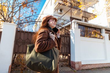 Beyaz tenli, paltolu ve bereli güzel bir kadının sokaktaki akıllı bir telefondan seslenişi. Alt görünüm.