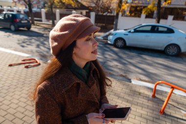 Dişlerinde diş teli olan, gülümseyen ve akıllı telefonu sokakta tutan beyaz bir kadının orta fotoğrafı. Şehir yaşam tarzı. Üst görünüm.