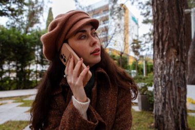 Şapkalı ve paltolu güzel beyaz bir kadının telefonda konuşmasının yan görüntüsü. Modern iletişim ve iş