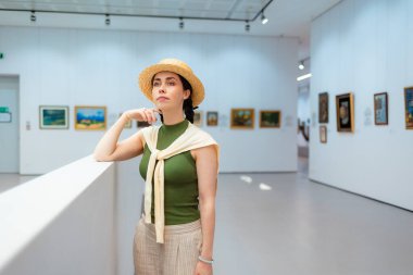 Sanat galerisinde saman şapkalı, genç, beyaz, zarif bir kadının poz verişi. Yan görüş. Kültürel eğitim kavramı.