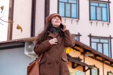 Dişlerinde diş teli olan, paltosu ve şapkası olan, sokakta duran güzel, beyaz, mutlu bir kadının alt manzarası. Orta atış. Yaşam tarzı ve şehir hayatı.