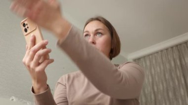 Genç, yetişkin, beyaz bir kadının oturma odasındaki akıllı telefondan duygusal iletişim kurduğu görüntüler. Video çağrısı ve sosyal medya kavramı.