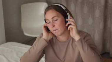 Odasında müzik dinleyip şarkı söyleyen, kulaklıklı, beyaz, genç bir kadının portresi. Üst Manzara. Ev eğlencesi..