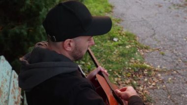 Yetişkin, yakışıklı, beyaz bir adamın gitar çalarkenki görüntüsü. Müzik aleti çalmayı öğreniyorum. Açık hava..