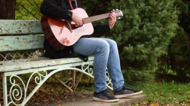 Tanınmayan bir adam sonbahar parkında bankta gitar çalıyor. Bacaklarını kapat. Gitar çalmayı öğreniyorum..
