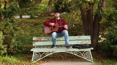 Kafkasyalı sakallı bir gencin, parktaki bankın tepesinde gitar çaldığı geniş bir çekim. Gitar çalmayı öğreniyorum..