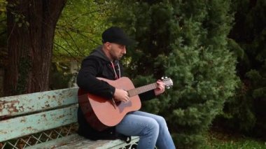 Genç beyaz, yakışıklı, sakallı adam parkta gitar çalıyor. Gitar çalmayı öğreniyorum.