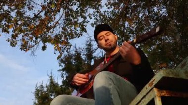 Yetişkin, beyaz bir adamın gitar çalarken tellerini parmaklamasının alt görüntüsü. Güneşli bir ışık. Bir müzik aleti çalmayı öğrenmek