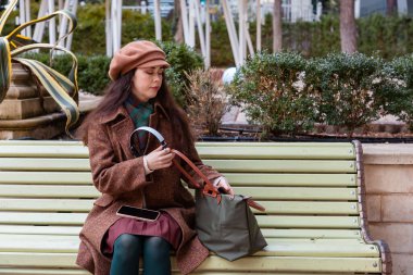 Kafkasyalı, şapkalı ve paltolu güzel bir kadının orta pozu çantadaki kulaklıkları alıp parkta bankta oturuyor. Sadece müzik rahatlığı..