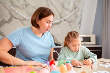 Küçük sevimli bir beyaz kız ve annesi Paskalya bahar tatili için kağıt tavşanlar süslüyorlar. Aile süitleri bir masada ve bayramlık Paskalya süslemeleri yapar..