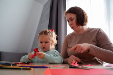 Kafkasyalı genç anne ve küçük tatlı kızının masa başında oturan kağıt kalpli kağıt kalplerini alt açıyla görmesi. Aile Sevgililer Günü kutlaması için hazırlanıyor..