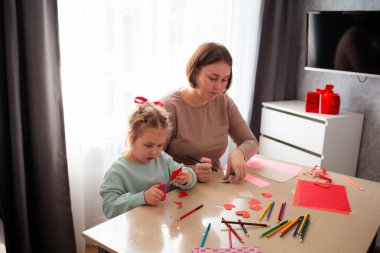 Kafkasyalı bir anne ve küçük tatlı kızının kağıt kalpler çıkardığı bir fotoğraf. Aile Sevgililer Günü kutlamasına hazırlanıyor..