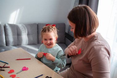 Kafkasyalı anne ve küçük tatlı kızın kağıt kesilmiş kırmızı kalplerle oynamaları. Sevgililer Günü kutlaması kavramı.