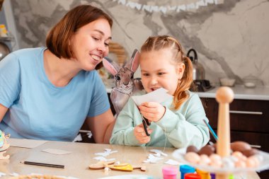 Mutlu yetişkin beyaz anne portresi ve onun küçük sevimli kızı ev için dekorasyon yapmak için kağıt kesiyor. Aile masada oturuyor. Bahar Paskalya tatili.