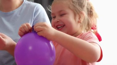 Annesiyle birlikte neşeli bir şekilde balon şişiren mutlu, küçük beyaz bir kız. Anaokulu çocuklarına öğretmenlik yapıyor. Anneler Günü konsepti.
