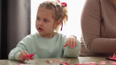 Küçük kız ve anne, kağıt sevgililer günü kartlarını makasla kesiyorlar. Sevgililer Günü ve Anneler Günü Kutlamaları