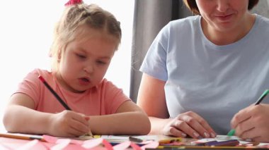 Genç bir kadın ve gülümseyen beyaz bir kız. Kağıttan sevgililer günü kartı çiziyor. Okul öncesi çocuk eğitimi. Sevgililer Günü ve Anneler Günü Kutlamaları.