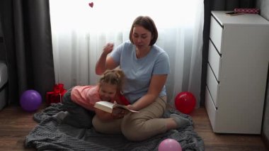 Anne ve beyaz bir kız birlikte masal kitabı okuyorlar. Orta atış. Anneler Günü ve anaokulu eğitimi kavramı.