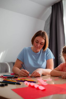 Genç anaokulu öğretmeni bir kıza tatil için nasıl kartpostal çizileceğini öğretiyor. Beyaz kadın ve küçük kız birlikte vakit geçiriyorlar. Dikey