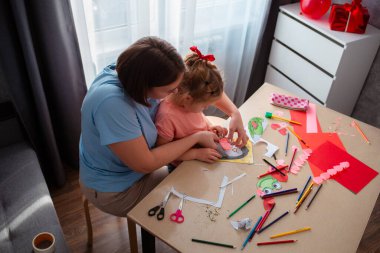 Kafkasyalı annelerin oynadığı ve küçük kıza anneler günü ve sevgililer günü için kartpostal yapmayı öğrettiği en iyi manzara. Aile masada oturuyor. Okul öncesi eğitim.