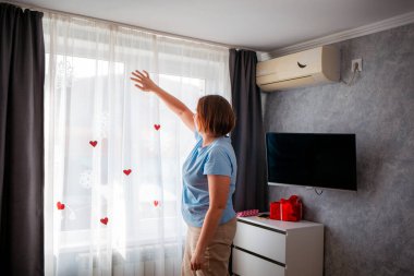 Beyaz perdeleri camında kırmızı kağıt kalpler olan beyaz bir kadın. Sevgililer Günü ve Anneler Günü için kutlama.