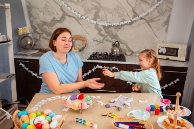 Kafkasyalı genç anne ve küçük tatlı kızının mutfakta Paskalya süslemeleri olan bir masada birlikte oynamalarının geniş bir görüntüsü..