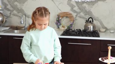 Anne ve küçük komik kızının orta fotoğrafı mutfak masasını ev yapımı kağıt bir çelenkle süslüyor. Paskalya için şenlikli hazırlıklar.