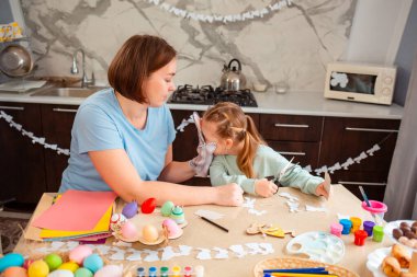 Kafkasyalı anne ve mutlu küçük kız masada oturup Paskalya için el işleri ve süslemeler yapıyorlar..
