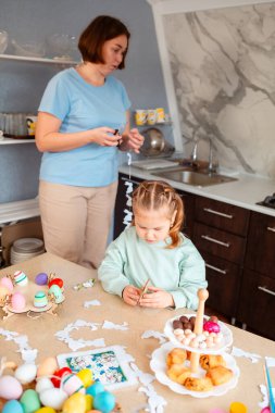Küçük bir kızın tahta tavşanla oynadığı, bahar için süslenmiş masada oturduğu bir sahne.