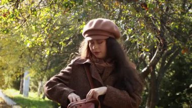 Paltolu ve şapkalı genç bir beyaz kadın parkın ortasında dururken çantasında bir şey arıyor..