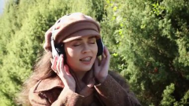 Beyaz bir kadının portresi. Paltosu ve şapkası olan, müzik dinleyen ve dans eden mutlu bir kadın. Arka planda yeşil ağaçlar. Zevk, mutluluk ve neşe ifadeleri.