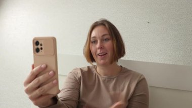 Beyaz tenli mutlu bir kadının akıllı telefondaki videoyla iletişim kurduğu bir fotoğraf. Video çağrısı ve sosyal medya kavramı.