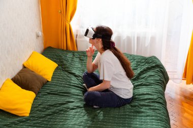 Evde VR kulaklık kullanan teknoloji düşkünü bir kadın akıllı eğlence sistemleriyle etkileşim içinde. Yan görünüm.