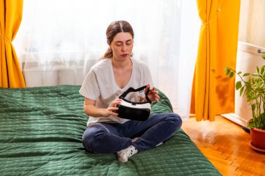 Fütüristik teknolojiyi deneyimleyen bir kadın, evinde yatakta oturmuş, yeni nesil eğlence çözümlerini test ediyor. Orta çekim.