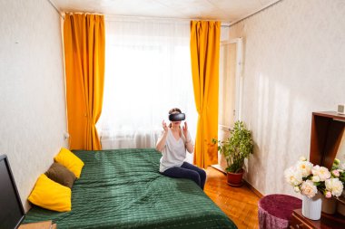 Gündelik ev ortamında, yatağında derin bir sanal gerçeklik deneyimi yaşayan son teknoloji ürünü metaevren teknolojisiyle uğraşan bir kadın. Geniş açı. Üst görünüm.