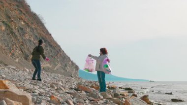 Gönüllüler kirliliği önlemek ve doğayı yeniden canlandırmak için okyanus kıyısı boyunca çöp topluyor. İnsanlar vahşi yaşamı korumak için koruma çabasına girişirler. Kadınlar fotoğraf çeker. Geniş açı.