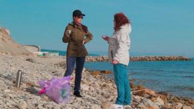 İki kadın çevreci, okyanus kirliliğini önlemek için plajları temizlemek ve diğer atıkları toplamak için birlikte çalışıyor. Kadınlar bir fren yapar ve çay içerler. Tam boy çekim.