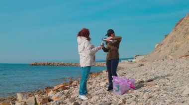 Kadın eylemciler kirliliği önlemek ve sorumlu atık imhası için kıyı şeridindeki çöpleri temizliyorlar. Kadınlar bir fren yapar ve çay içerler. Tam boy çekim.