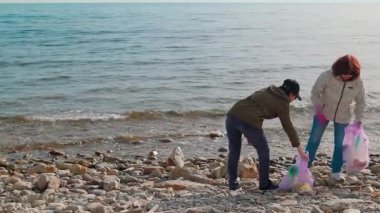 Uzak bir sahil şeridinden çöp toplayan iki kadın, ekolojik bir felaketi önlüyor ve çevre sorumluluğunu destekliyor. Gönüllüler fotoğraf raporu alıyor.