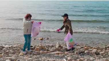 İki çevreci, kirliliği azaltmak ve vahşi yaşamı korumak için kirlenmiş bir plajı plastik ve diğer atıkları toplayarak temizliyor. Gönüllüler okyanusu kirlenmekten kurtarmak için çalışıyorlar. Yan görünüm.