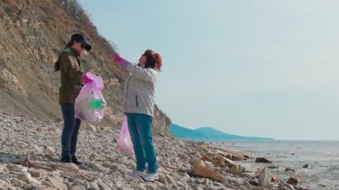 İki gönüllü kadın, okyanus kirliliğini önlemek ve vahşi yaşamı korumak için sahilden çöp topluyor. İnsanlar Dünya Günü çevre temizleme girişimine katılıyor. Tam boy çekim.